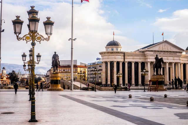 Tiled square with equestrian statues near lanterns and aged building facade with columns in Yugoslavia